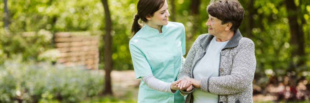 Hébergement senior : une personne âgée se promène joyeusement dans un jardin avec son accueillant.