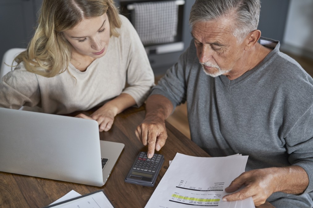 Un homme senior et une jeune femme utilisant un ordinateur et une calculatrice pour planifier le financement des frais d'obsèques.